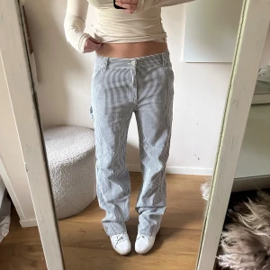 Randiga raka byxor i bomull - Säljer ett par vita och grårandiga byxor med raka ben och normal passform. Jag är 175! Byxorna har klassisk midja, bälteshällor och sidofickor. Perfekta för dig som gillar en chill och stilren look. Materialet är mjuk bomull som känns skönt mot huden.