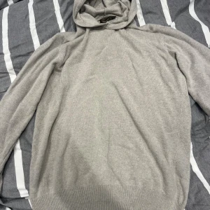 Ljusgrå hoodie i kashmir från Oscar Jacobson - Mjuk och lyxig ljusgrå hoodie från Oscar Jacobson i kashmir. Tröjan har en klassisk huva, ribbade muddar och lång ärm. Perfekt för dig som gillar stilren och bekväm design med exklusiv känsla. Hoodien har använts några gånger men har inga defekter nypris 1799 mitt pris 849