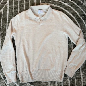Beige pikétröja i bomull från Bläck - Snygg beige pikétröja från Bläck i mjuk bomull. Tröjan har klassisk krage, lång ärm och ribbade muddar vid ärmslut och nederkant. Perfekt för en clean och stilren look, funkar året runt och är lätt att matcha med jeans eller kostymbyxor. 