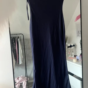 Marinblå långklänning med smala axelband - En stilren marinblå långklänning med smala axelband och figurnära passform. Klänningen är ärmlös och har en enkel, elegant siluett som passar perfekt för dig som gillar minimalistisk stil.
