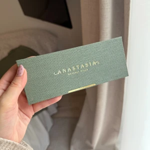 Anastasia Beverly Hills Nouveau Palette - Snygg ögonskuggspalett från Anastasia Beverly Hills i modellen Nouveau. Paletten har 12 olika nyanser, både matta och skimriga, i färger som lila, guld, grönt, brunt och nude. Förpackningen är i grönt tyg med gulddetaljer och spegel på insidan.