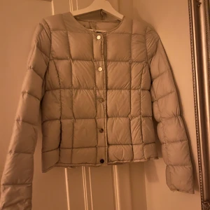 Beige quiltad pufferjacka från Å - Säljer en beige, quiltad pufferjacka från Åhléns i storlek XS. Jackan har rund halsringning, tryckknappar framtill och ett stilrent rutmönster. Perfekt för dig som gillar minimalistisk och clean stil.