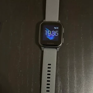 Grå smartklocka Garmin med silikonband - Säljer en snygg grå smartklocka från Garmin med fyrkantig display och mjukt silikonarmband. Klockan har digital skärm med tydlig tidvisning och erbjuder 100 tals olika smarta funktioner. Perfekt för dig som gillar teknik och vill ha koll på din vardag.