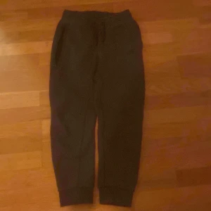 Svarta mjukisbyxor från Nike - Svarta mjukisbyxor från Nike med dragsko i midjan och ribbade muddar vid bensluten. Byxorna har två sidofickor och en diskret Nike-logga på ena benet. Perfekta för chill eller träning.