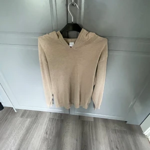 Beige hoodie Kashmir  - Säljer en stilren beige hoodie som är Kashmir. Tröjan har huva, långa ärmar och ribbade muddar vid ärmslut och nederkant. Perfekt för en chill och avslappnad look.