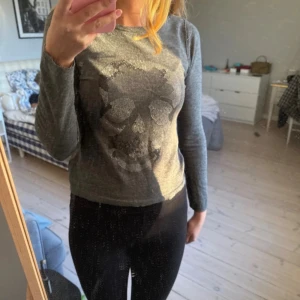 Grå långärmad tröja med döskalle - Grå långärmad tröja med ett stort döskallemotiv framtill i små silvriga nitar. Den har sytts fram till som på sista bilden och har ett litet litet hål på ryggen som behövs sys