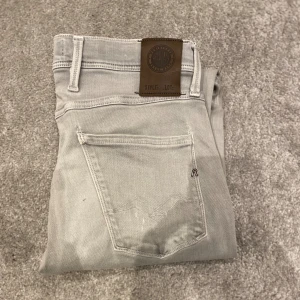 Replay Anbass Jeans - Säljer ett par ljusgrå jeans från Replay med klassisk femficksdesign och snygga detaljer på bakfickorna. Jeansen har slim fit-passform och är tillverkade i mjukt jeansmaterial med stretch. Perfekta för dig som gillar stilrena och bekväma byxor.