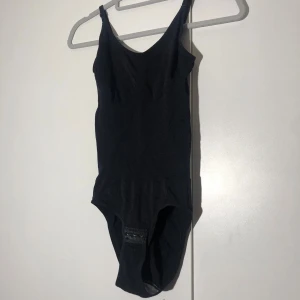 Svart ribbad bodysuit med smala axelband - Svart tajt bodysuit som ska forma midjan. Längd ca 70cm. Pris: 10kr 