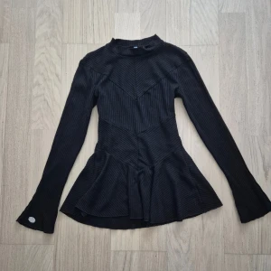 Finstickad svart ribbad tröja - Svart tröja som är utsvängda nedtill och har vida ärmar med en silvrig logga på ena ärmslutligen som en fin detalj #peplumtröja #polotröja #flare 