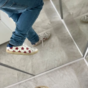 Saint Laurent sneakers med röda stjärnor - Snygga vita sneakers från Saint Laurent med röda stjärnor på sidorna och blå häl. Skorna har snörning, platt sula och rund tå. Tillverkade i skinn med slitstark gummisula. Perfekt för dig som gillar att sticka ut med coola detaljer.