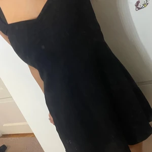 Svart ribbad kortklänning med v-ringning - Supersnygg svart kortklänning med ribbad struktur och v-ringad hals. Klänningen har korta ärmar och en lätt utställd passform som ger en feminin siluett. Detalj med rynkning vid bysten för extra stilpoäng. Perfekt för dig som gillar enkel men trendig look.