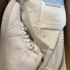 Nike Jordan 1 helvita sneakers - Säljer ett par fräscha och helt oanvända Nike Jordan 1 sneakers i helvitt skinn med snygga detaljer och klassisk snörning. Modellen har en rund tå och platt sula, perfekt för dig som gillar stilrena och ikoniska sneakers. Levereras i originalkartong med papper.