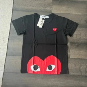 Svart CDG T-shirt med hjärta - Skitsnygg T-shirt från Comme Des Garçons i svart med rött hjärta nertill. Tröjan är helt oanvänd och nyskick! Pris: 799 | Tveka inte att höra av er med prisförslag eller funderingar!
