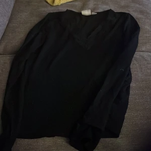 Svart långärmad blus med spets - Säljer en svart långärmad blus med v-ringning och spetsdetaljer vid halsen. Blusen har en klassisk och stilren look som passar perfekt till jeans eller kjol. Enkel att matcha och superbekväm att bära.