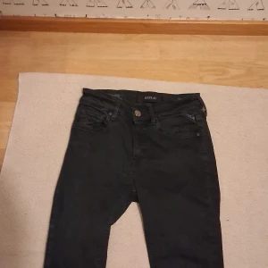 Svarta Replay jeans  - Säljer ett par svarta jeans från Replay med klassisk femficksdesign och raka ben. Jeansen har bälteshällor, knapp och dragkedja framtill samt diskret Replay-logga på bakfickan. Perfekta för dig som gillar stilrena och tidlösa jeans. Storlek w27.