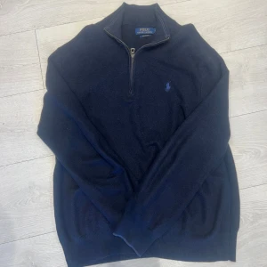 Marinblå stickad tröja Polo Ralph Lauren - Snygg marinblå stickad tröja från Polo Ralph Lauren i mjuk pima bomull. Tröjan har half zip-dragkedja, långärmad design och den klassiska broderade loggan på bröstet. Perfekt för dig som gillar stilrena och tidlösa plagg. Storlek M men passar S