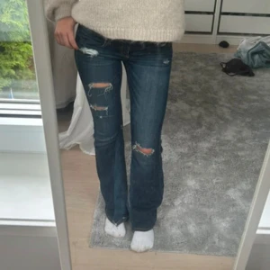 Hollister jeans  - Säljer ett par mörkblå bootcut jeans med slitna detaljer och hål på låren. Jeansen har snygga broderade bakfickor med kontrastsömmar och låg midja. Materialet är klassisk denim och passformen är normal. Perfekta för dig som gillar en avslappnad och trendig look. Waist 24, length 31❤️