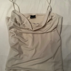 Beige linnetopp från Gina Tricot - Säljer en stilren beige linnetopp från Gina Tricot med tunna axelband och snygg draperad urringning. Toppen är i ett mjukt, slätt material som känns skönt mot huden och har en enkel, clean look som passar till många outfits.