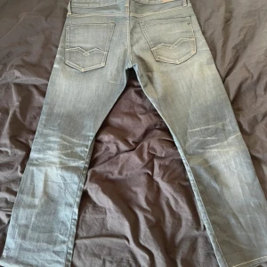 Replay jeans blå straight fit 36/30 - Säljer ett par blå Replay jeans i straight fit med klassisk femficksdesign och snygga detaljer på bakfickorna. Jeansen har ljus tvätt och tydliga slitningar för en cool look. Materialet är jeans med skön känsla och passformen är normal.