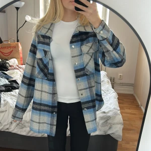Blå och grå rutig overshirt från LinDEX - Overshirt från LinDEX i blått, grått och svart rutigt mönster. Skjortan har två stora bröstfickor med lock, knappar framtill och klassisk krage. (Använt några fåtal gånger) 