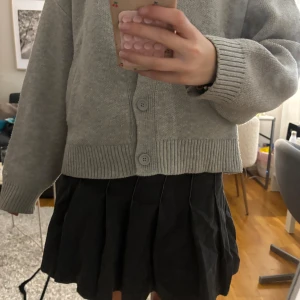 Svart plisserad jeanskjol - Säljer en svart kort plisserad kjol i jeansmaterial. Kjolen har tydliga sömmar och knäppning i midjan. Perfekt för dig som gillar en trendig och avslappnad stil. Passar till många olika outfits och är superenkel att styla.