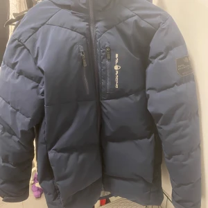 Marinblå Sail Racing dunjacka - Säljer en marinblå dunjacka från Sail Racing då jag tänkte köpa en annan jacka. Har haft jackan sen slutet av förra vintern. Är inte trasig har inga sprickor i sömmen