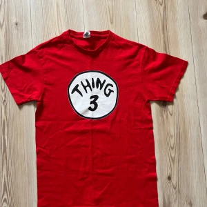 Röd Thing 3 t-shirt i bomull - S - Röd t-shirt med tryck 'Thing 3' i svart och vitt på bröstet. Klassisk rund hals och korta ärmar. Tillverkad i 100% bomull för en skön och mjuk känsla. Perfekt för dig som gillar statement-plagg och vill sticka ut lite extra.