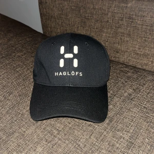 Svart och vit keps från Haglöfs - Två stilrena kepsar från Haglöfs, en svart och en vit, båda med böjd skärm och justerbar passform. Kepsarna har Haglöfs logga framtill i kontrasterande färg och är tillverkade i ett slitstarkt material som passar perfekt till vardagslooken.