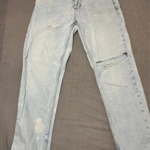 Ljusblå slitna jeans i storlek 31/30 - Ljusblå jeans med slitningar och hål på benen, i klassisk tvättad denim. Modellen har raka ben och en avslappnad look med tydliga slitdetaljer. Perfekta för dig som gillar en trendig och avslappnad stil.