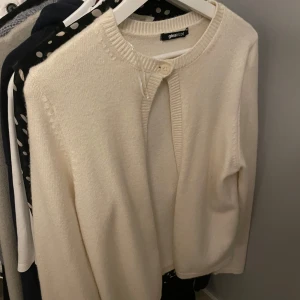 Krämvit kofta från Gina Tricot - Superfin krämvit kofta från Gina Tricot med rund halsringning och en enkel knapp framtill. Koftan är stickad i mjukt material och har långa ärmar. Perfekt att slänga över en topp för en clean och stilren look.