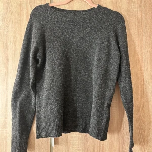 Mörkgrå stickad tröja från Vero Moda - Mysig mörkgrå stickad tröja från Vero Moda i enkel och klassisk modell. Tröjan har rund halsringning, långa ärmar och ribbade muddar vid ärmslut och nederkant. Perfekt för lager-på-lager under kyliga dagar.