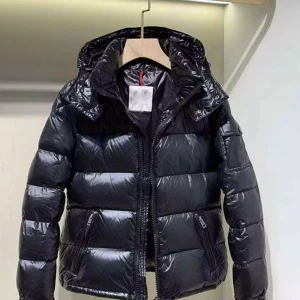 Svart pufferjacka från Moncler - Snygg svart pufferjacka från Moncler med glansig finish och huva. Jackan har dragkedja framtill, två fickor med dragkedja och klassisk Moncler-logga på ärmen. Perfekt för kalla dagar när du vill hålla stilen och värmen.