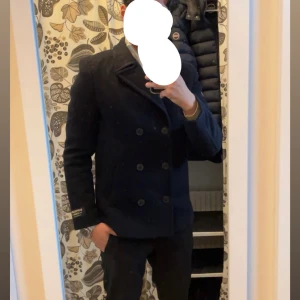 Superdry skepparkavaj - Säljer en stilren mörkblå skepparkavaj från Superdry med klassisk dubbelknäppning och bred krage. Jackan har en insydd quiltad innerdel med dragkedja, vilket ger en modern look. Vid snabb affär kan priset diskuteras. Nypris 2499kr mitt pris 1799kr använd ett fåtal gånger så skicket är som nytt