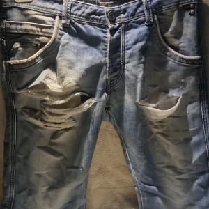 Ljusblå slitna jeans från Bragg - Ljusblå jeans från Bragg med rejält slitna och trasiga detaljer framtill. Jeansen har klassisk femficksdesign, normal passform och är tillverkade i denim. Perfekt för dig som gillar en edgy och avslappnad stil.