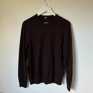Mörkbrun ulltröja från Uniqlo - En stilren mörkbrun tröja från Uniqlo i 100% ull. Klassisk rund halsringning och långärmad modell, perfekt för lager-på-lager under kyliga dagar. Enkel och clean design som funkar till det mesta. 3Q18
