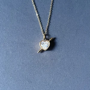 Rebel Heart – Golden Frost - Guldpläterat halsband i rost- och nickelfritt stål. Vitt hjärta med pil. Kedja 50 cm, justerbar. Hängets diameter 0,9 cm.