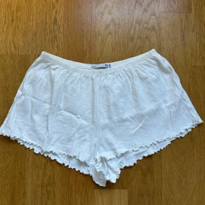 Vita ribbade shorts från 157 - Säljer ett par vita shorts från 157 i storlek M. De har ribbad struktur med diskreta vertikala ränder och en elastisk midja. Kanterna är vågiga och ger en söt touch. Perfekta för varma dagar och chill hemma.