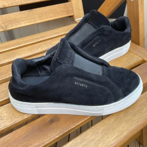 Svarta sneakers från Axel Arigato - Svarta sneakers från Axel Arigato i mocka med vit platt sula.Har en liten defekt som man inte tänker på när man har skorna på,därav priset!Såklart äkta.Modellen är aregato laceless.Pris går att diskutera!✅
