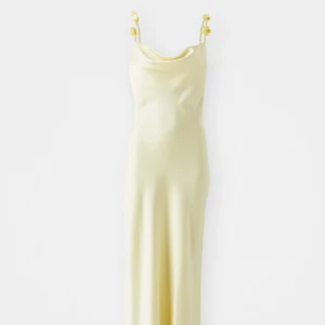 Ljusgul långklänning från Gina Tricot - Supersnygg ljusgul långklänning från Gina Tricot med tunna axelband dekorerade med blommor. Klänningen har en mjuk satinliknande yta och öppen rygg. Endast använd en gång, storlek S. skriv för fler bilder