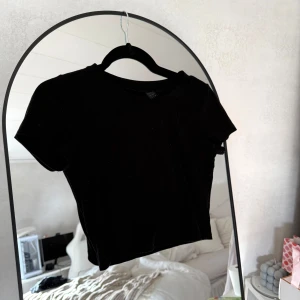 Svart croppad ribbad topp - En svart croppad topp med korta ärmar och rund hals. Toppen är ribbad och har en tight passform som sitter snyggt på kroppen. Lite nopprig, se andra bilden.