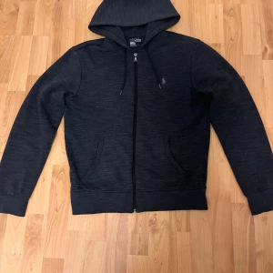 Mörkblå hoodie från Polo Ralph Lauren - Snygg mörkblå hoodie från Polo Ralph Lauren med dragkedja, huva med snörning och två fickor framtill. Använd 1 gång och är som ny men utan prislapp.