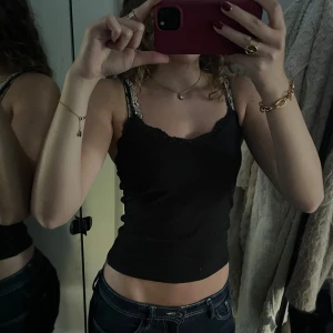 Svart spetslinnetopp från H&M - Svart linne från H&M med smala axelband och snygg spetskant upptill. Modellen är croppad och sitter tight mot kroppen. 