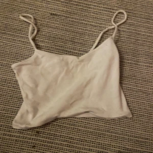 Vit ribbad linnetopp från Monki - Säljer en vit ribbad linnetopp från Monki i storlek XXS. Toppen har tunna axelband och är tillverkad i mjuk bomullsmix. Perfekt att matcha med jeans eller kjol för en chill look.