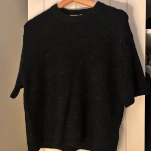 Svart stickad tröja med kort ärm - Mysig svart stickad tröja med korta ärmar och rund hals. Perfekt för lager-på-lager och passar till både jeans och kjol. Tröjan har en lite lösare passform och är superenkel att styla för en chill look.
