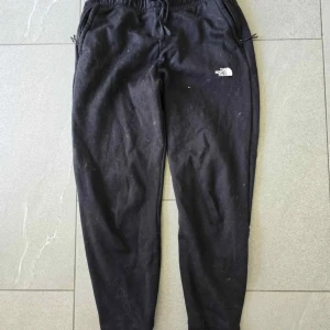 Svarta mjukisbyxor The North Face - !!Obs katten har legat på dessa i garderoben därav allt hår, jag kommer rolla bort det vid köp!!Svarta mjukisbyxor från The North Face med dragsko i midjan och fickor med dragkedja. Byxorna har en slim passform och är perfekta för chill eller träning. Loggan är tryckt på vänster lår. Sköna och stilrena byxor för en avslappnad look.