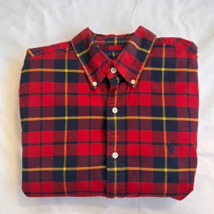 Rutig röd skjorta från Ralph Lauren - Säljer en slim fit rutig skjorta från Ralph Lauren i rött, blått och gult. Skjortan är i stretchig bomull, har långa ärmar, klassisk krage och knäppning framtill. Ikoniska Polo-loggan broderad på bröstet. Perfekt för dig som gillar stilren och färgstark look. Nypris: 1700kr💯✅