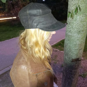 Cool läderhatt - Cool svart keps i läder/skinn med bred skärm och paneldesign. Insidan är fodrad med glansigt brunt satinmaterial för extra komfort. Perfekt accessoar för dig som vill sticka ut med en unik och stilren look. Har inga defekter. Färgen är väldigt mörk brun nästan svart. Kp vid fler frågor❤️