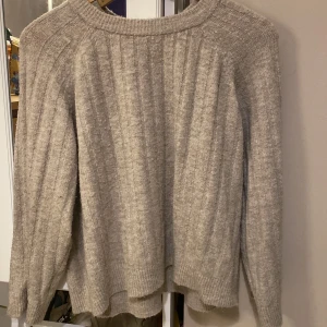 Beige stickad tröja från 157, S - Mysig beige stickad tröja från 157 i storlek S. Tröjan har ribbade detaljer, rund halsringning och långa ärmar med relaxed fit. Perfekt för lager-på-lager och chill höst- eller vinterstil.