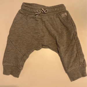 Grå mjukisbyxor med snörning - Grå mjukisbyxor från Lindex med ribbade muddar, snörning i midjan och två fickor fram. Byxorna är tillverkade i mjukt bomullsmaterial och har en avslappnad passform, perfekta för chill dagar.