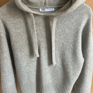 Beige stickad hoodie från Zara - Mysig grå stickad hoodie från Zara med huva och snörning. Tröjan har ribbade muddar och är perfekt för dig som gillar en enkel men stilren look. Passformen är normal och materialet känns mjukt och skönt mot huden.